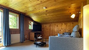 Ein gemütliches Blockhauss-Interieur mit einer Couch, einem Fernseher und einem Esstisch.