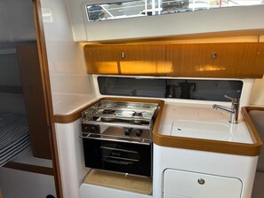 Eine kleine Kombühe mit Kochfeld, Backofen, Spüle und Holzsärchen.