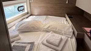 Un lit compact avec du linge de lit blanc et des oreillers, une fenêtre donnant sur un beau paysage et une petite table de chevet équipée d’une prise électrique.