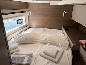 Ein gemütliches Bett mit weißen Leinen und Kissen, ein Fenster mit Blick und ein kleiner Nachttisch mit Steckdose.
