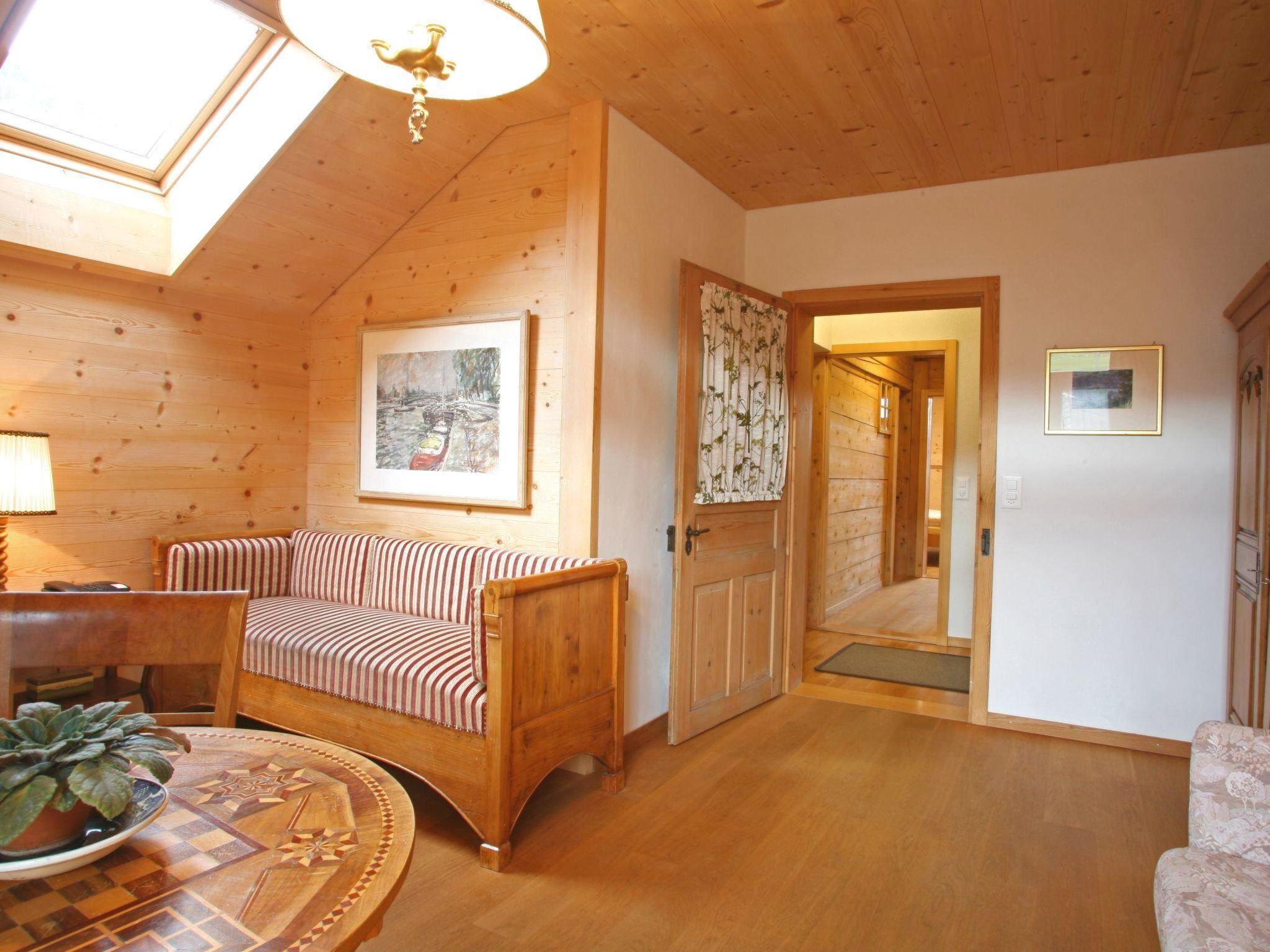 A cozy room with a wooden ceiling, a sofa, a table with a plant, and a door leading to another room.