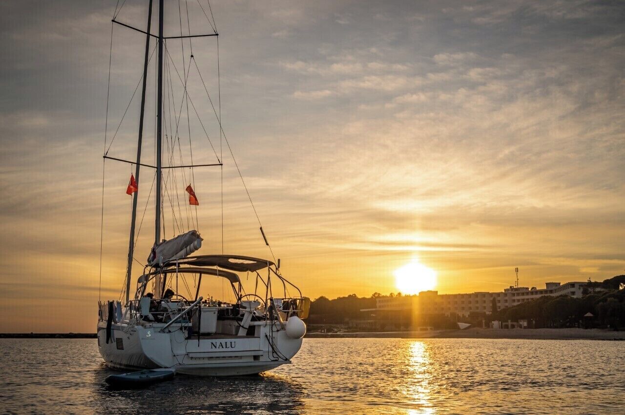 Ein Segelboot namens 'NALU' auf ruhigem Wasser bei Sonnenuntergang.