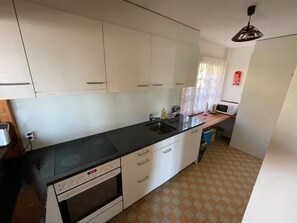 Een kleine keuken met witte kastjes, een zwart aanrecht en een magnetron.