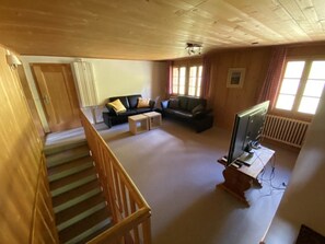 Een ruime woonkamer met een trap, een zithoek, een televisie en een radiator.