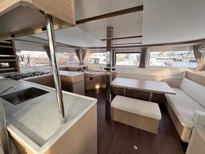 A compact kitchen with a sink, stove, and dining area with a bench and table. - Sun-Kissed Sailing Adventure in Islas Sarónicas (Alimos)