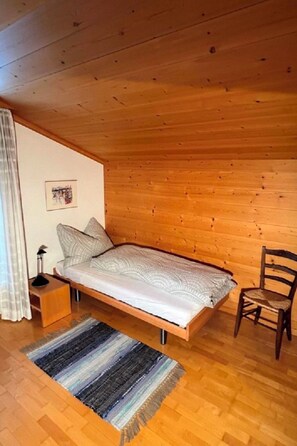 A single bed with a patterned bedspread in a room with wooden walls and flooring. - Oberland Nr. 19 Appartement/Fewo, Dusche oder Bad, WC 6-Bettwohnung by Interhome (Gstaad)