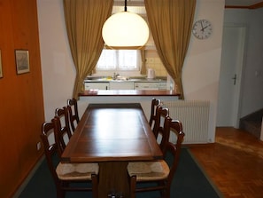 A dining area with a wooden table and chairs, a hanging light fixture, a kitchen area with a sink and stove, and a clock on the wall. - Oberland Nr. 19 Appartement/Fewo, Dusche oder Bad, WC 6-Bettwohnung by Interhome (Gstaad)
