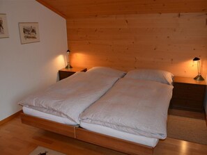 Un lit double avec un cadre en bois, deux tables de chevet et deux lampes fixées au mur.
