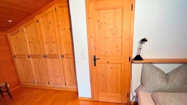 Huoneessa on puulattia, sohva, kuviollinen matto ja ovi.