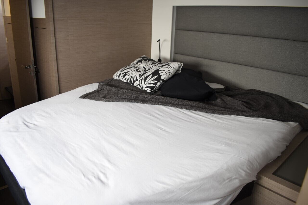 Una cama bien tendida con sábanas blancas, cabecera gris y almohadas con estampado blanco y negro.
