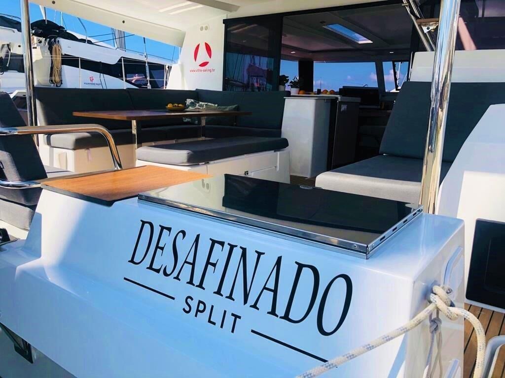 L’intérieur d’un yacht comprenant un espace repas, un coin salon et un logo bien visible : « DESAFINADO SPLIT ».