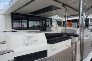 A yacht's deck with a seating area, a lifebuoy, and a logo. - Sun-Kissed Sailing Adventure in Islas Sarónicas (Alimos)