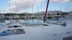 A marina with multiple boats docked, a clear sky, and mountains in the background. - Sun-Kissed Sailing Adventure in Islas Sarónicas (Alimos)