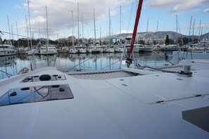 A marina with multiple boats docked, a clear sky, and mountains in the background. - Sun-Kissed Sailing Adventure in Islas Sarónicas (Alimos)