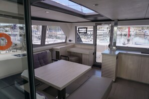 A modern interior with a dining area, a small kitchen, and a seating space with a view of the marina. - Sun-Kissed Sailing Adventure in Islas Sarónicas (Alimos)