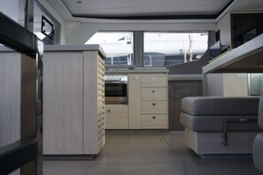 A compact kitchen with a built-in oven, a small refrigerator, and a seating area with a bench. - Sun-Kissed Sailing Adventure in Islas Sarónicas (Alimos)