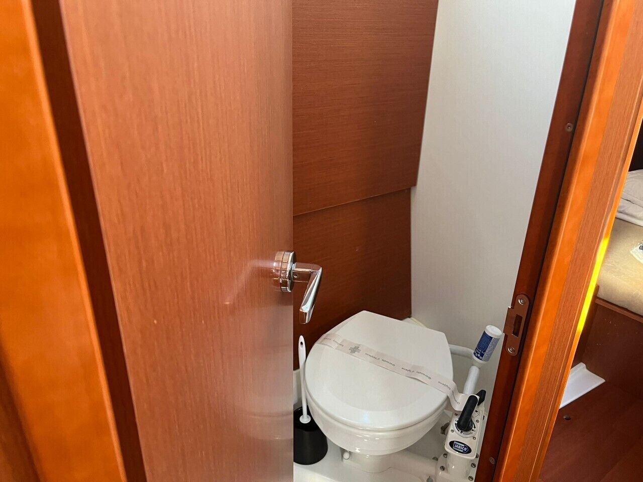 Un baño pequeño con un inodoro blanco, una puerta de madera y un estante con artículos de aseo.