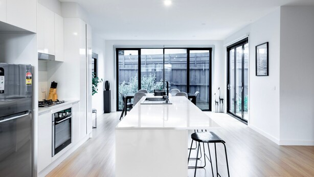 Een moderne keuken met een centraal eiland, een eethoek met een lange tafel en grote ramen.