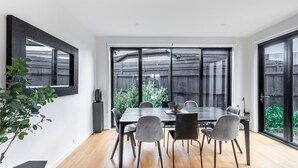 Een moderne eethoek met een grote tafel, zes stoelen en uitzicht op een houten schutting en groen.