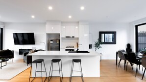 Een moderne keuken met witte kasten, een centraal eiland met krukken, een ingebouwde kookplaat en een flatscreen televisie boven het eiland.