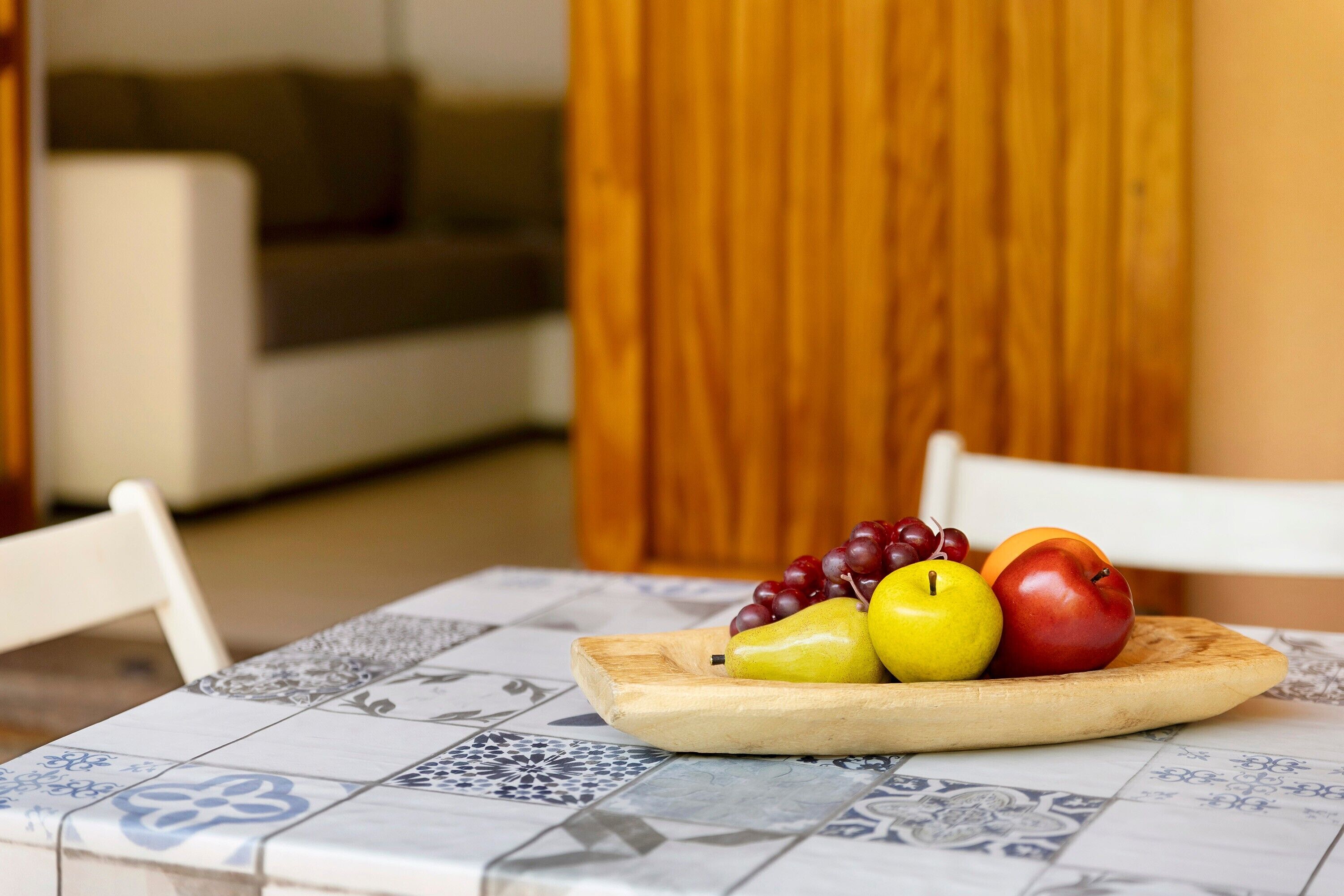 Una mesa de comedor con una bandeja de frutas, una silla blanca y un aparador de madera al fondo.