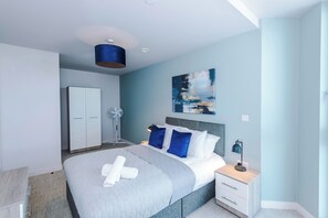 A modern bedroom with a bed, bedside table, nightstand, and a ceiling fan. - 1BDR Open Plan Apartment With Full Kitchen (Stretford)