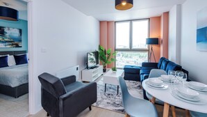 Ett modernt vardagsrum med en matplats, en platt-TV, en soffa, ett soffbord och utsikt över staden genom stora fönster.