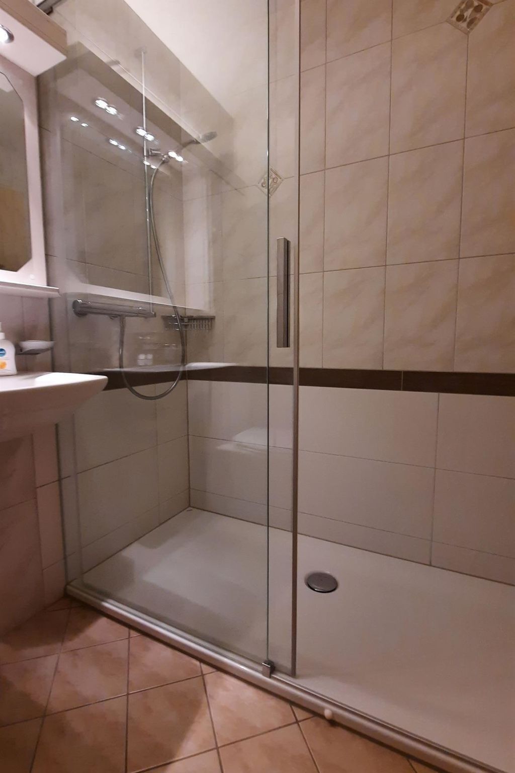 Une salle de bain moderne avec une douche à parois de verre, un lavabo blanc et un miroir au-dessus.
