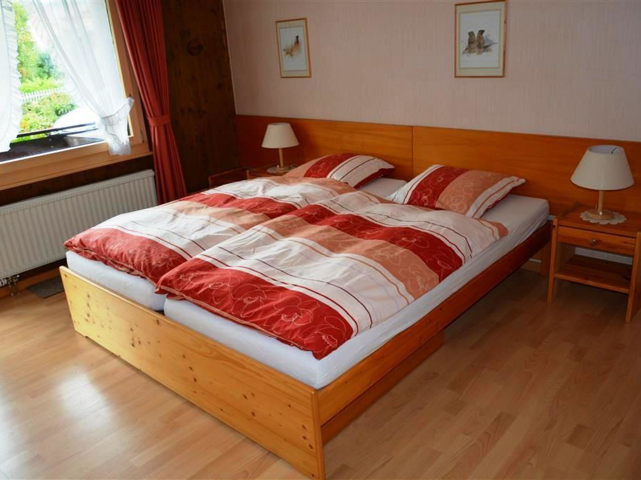 A wooden bed with a red and white bedspread, two bedside lamps, and framed pictures on the wall.