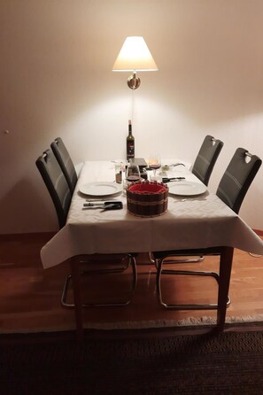 A dining table with a white tablecloth, four chairs, a candle, a wine bottle, and a basket. - Mösli (Zimmerli) Appartement/Fewo, Dusche oder Bad, WC 2-Bettwohnung by Interhome (Zweisimmen)