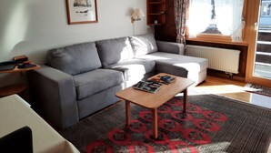 A modern living room with a grey sofa, a wooden coffee table, a patterned rug, a framed picture on the wall, and a window with curtains. - Mösli (Zimmerli) Appartement/Fewo, Dusche oder Bad, WC 2-Bettwohnung by Interhome (Zweisimmen)