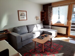 A modern living room with a grey sofa, a wooden coffee table, a patterned rug, a framed picture on the wall, and a window with curtains. - Mösli (Zimmerli) Appartement/Fewo, Dusche oder Bad, WC 2-Bettwohnung by Interhome (Zweisimmen)