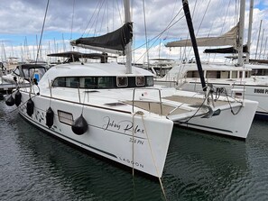 Eine weiße Yacht mit dem Namen 'Johnny Relax' liegt in einer Marina zusammen mit anderen Booten vor Anker.