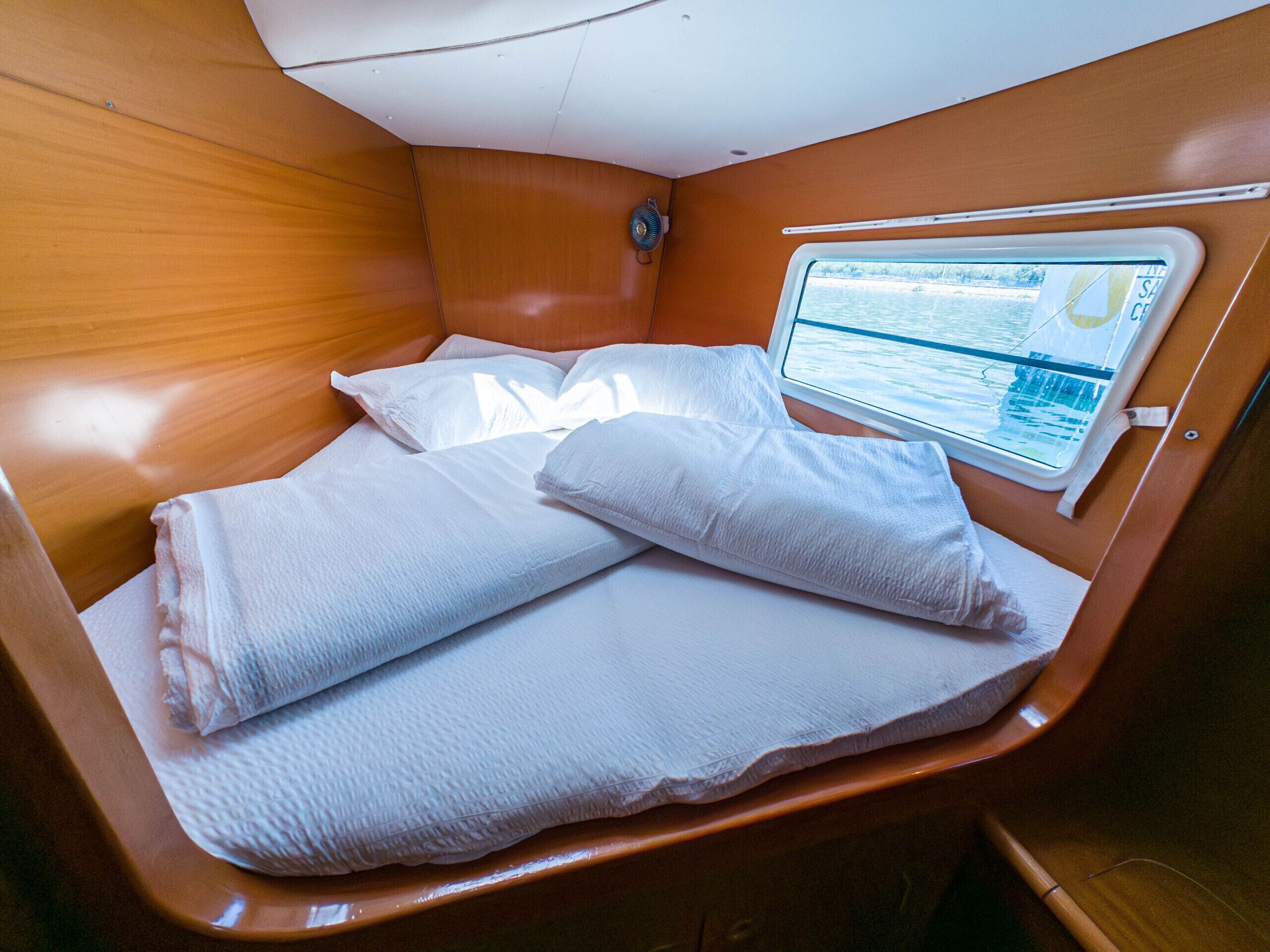 Une cabine équipée d’un lit, d’une fenêtre donnant sur l’eau et d’un ventilateur.