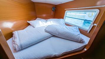 Une cabine équipée d’un lit, d’une fenêtre donnant sur l’eau et d’un ventilateur.