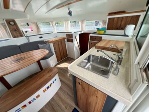 A compact kitchen with a sink, wooden cabinets, and a dining area with a bench. - Sun-Kissed Sailing Adventure in Northern Croatia (Punat)