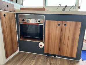 Eine kleine Küche mit Einbauofen, Holzschränken und einer Arbeitsplatte.
