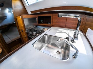 A compact galley with a stainless steel sink, a stove, and wooden cabinetry. - Sun-Kissed Sailing Adventure in Northern Croatia (Punat)