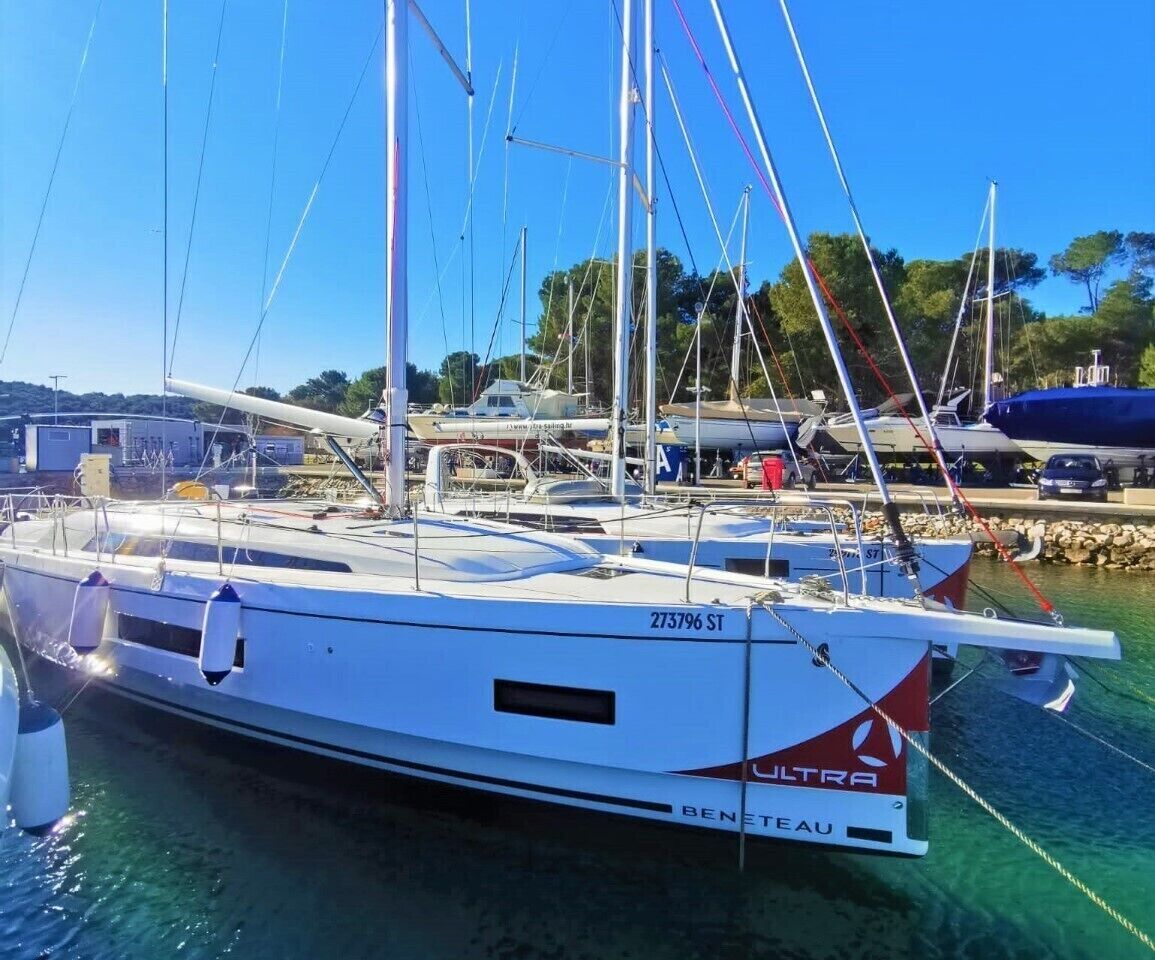 Eine Segelyacht vom Typ BENETEAU liegt in einer Marina, im Hintergrund weitere Boote.