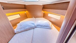Une cabine compacte et bien éclairée, dotée d’un lit avec une tête de lit et de deux oreillers, ainsi que d’une petite fenêtre située au-dessus du lit.