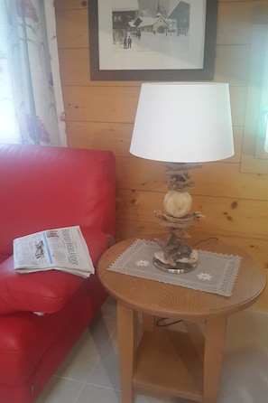 Una sala de estar con un sofá rojo, una mesa de madera con una lámpara y un cuadro en la pared.