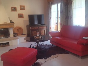Una sala de estar con un sofá rojo, un televisor sobre un mueble bajo, una chimenea y una ventana con cortinas.