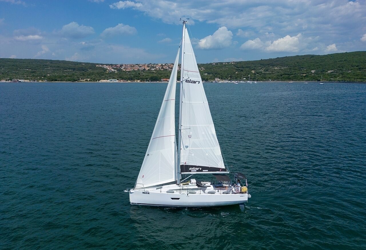 A sailboat on calm water with a hilly landscape in the background.