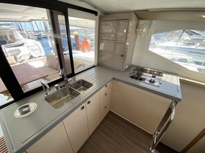 Une petite cuisine fonctionnelle, équipée d’un évier, d’une cuisinière et de placards, donnant sur un port de plaisance.