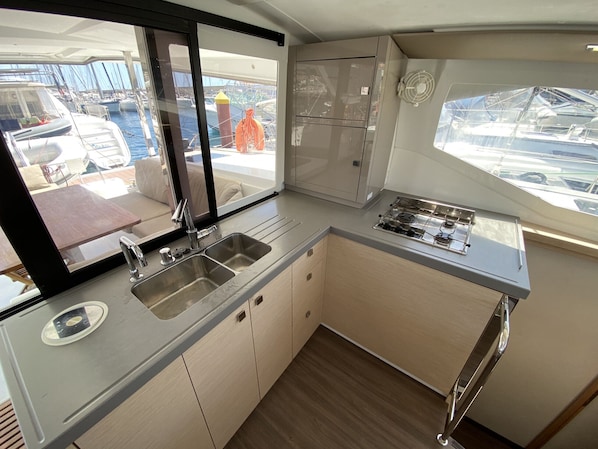 A compact galley with a sink, stove, and cabinets, overlooking a marina.
