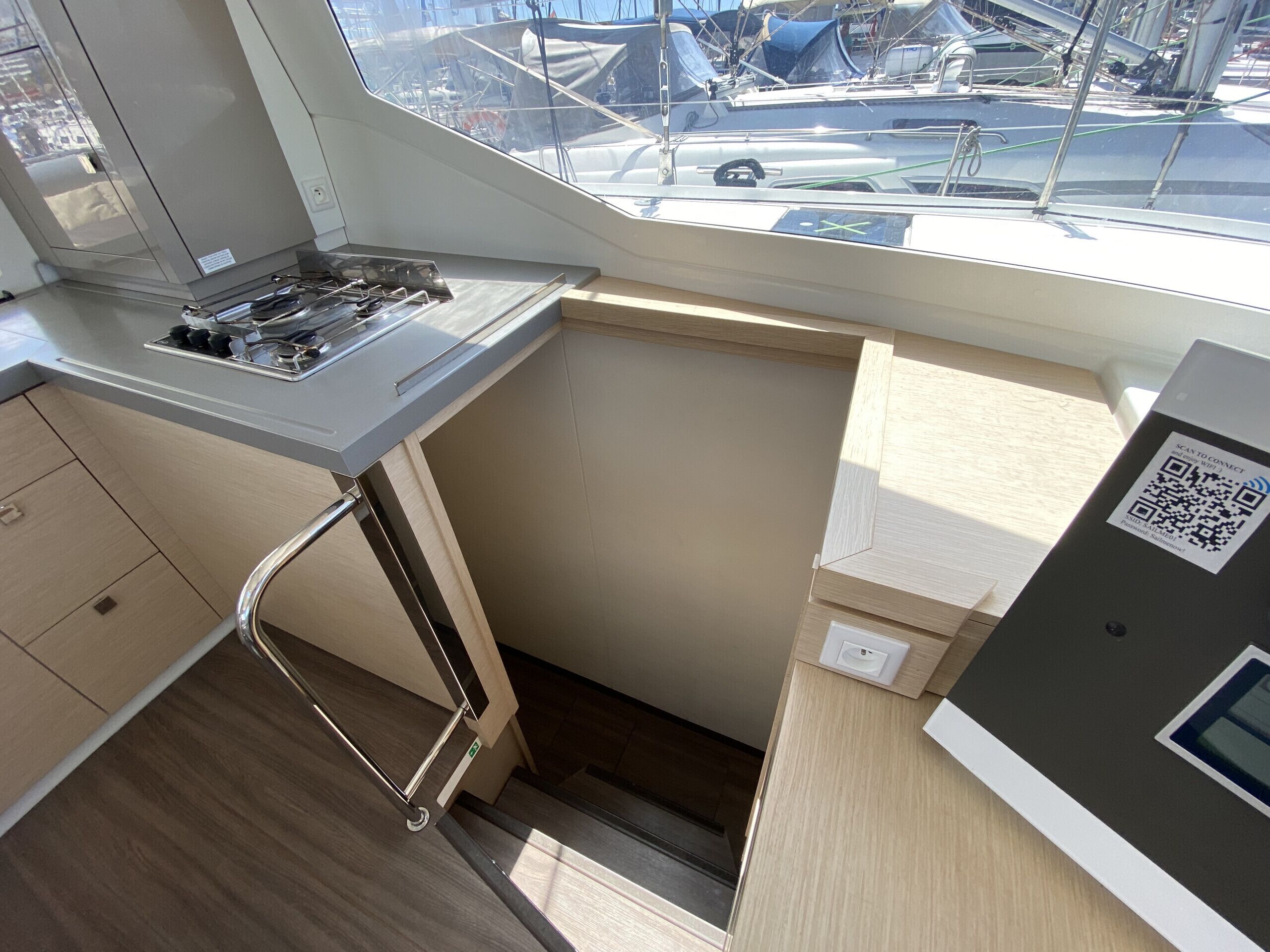 A compact galley with a stove, a small sink, and a window with a view of boats.