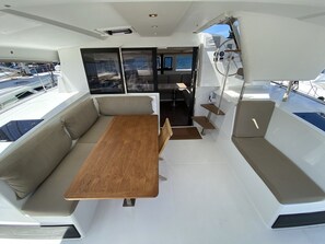 Das Interieur einer Yacht mit Holztisch, gepolsterten Sitzgelegenheiten und Blick auf den Yachthafen.