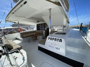 A boat deck with a seating area, a table, and a sign reading 'PAPAYA SAILME'.