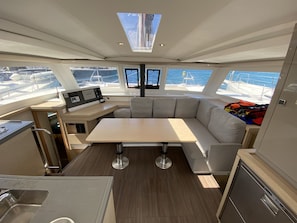 A yacht interior with a dining area, a control panel, and a view of the sea.