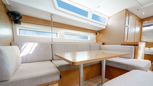 Ett kompakt och väl upplyst interiört utrymme med ett bord i mitten och bekväma sittplatser, stora fönster och en takfläkt.